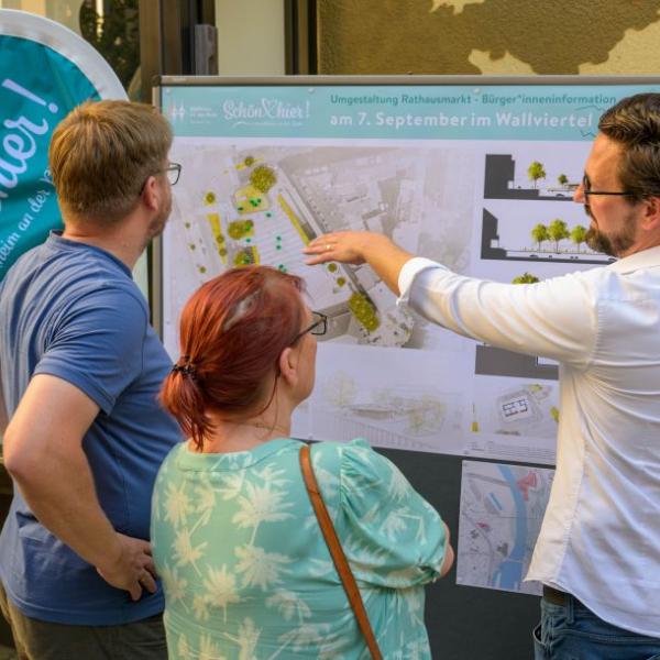 Einige Bürger*innen schauen sich die Planung des Rathausmarktplatzes auf einem Plakat an und lassen sich den Entwurf erläutern. | Foto: Walter Schernstein