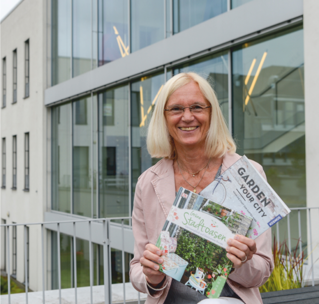 Frau vom Felde, Leiterin der Stadtbibliothek im Medienhaus, vor dem hinteren geäudeteil des Medienhauses mit zwei Büchern in der Hand