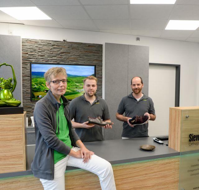 Auf dem Foto sieht man eine Frau und zwei Männer, die Schuhe in der Hand haben und ein Teil des Teams von Bausdorf Orthopädie bilden